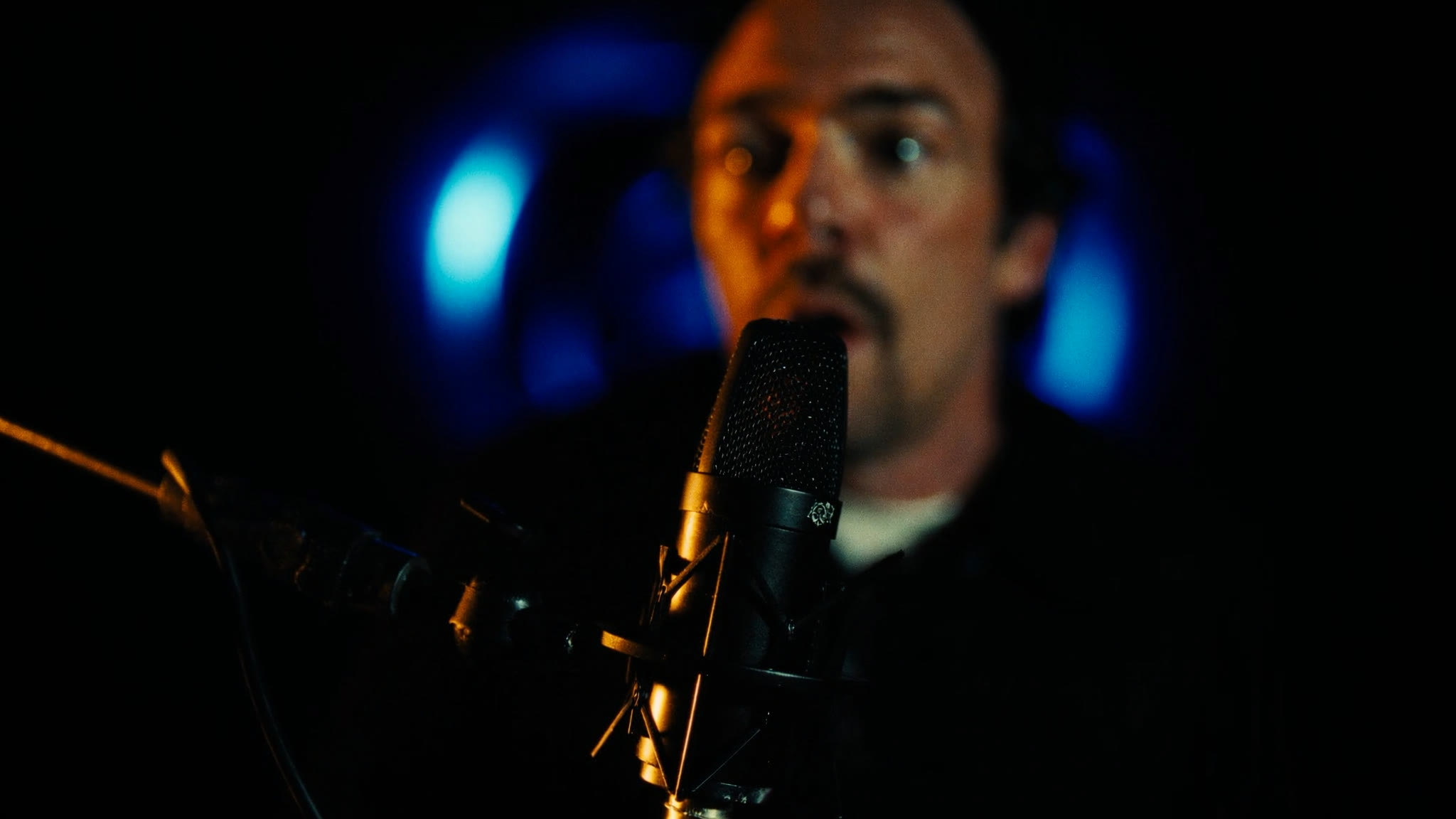 Close-up of a broadcast microphone with a speaker behind it
